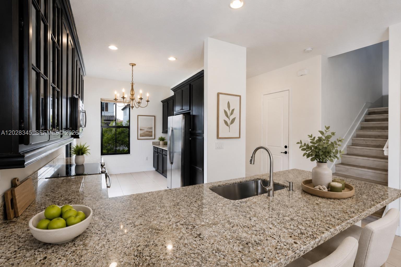 A kitchen features black cabinets, granite countertops, a central island with a sink, and stairs — 9717 W 34th Ln, Hialeah FL 33018, HIALEAH, FL