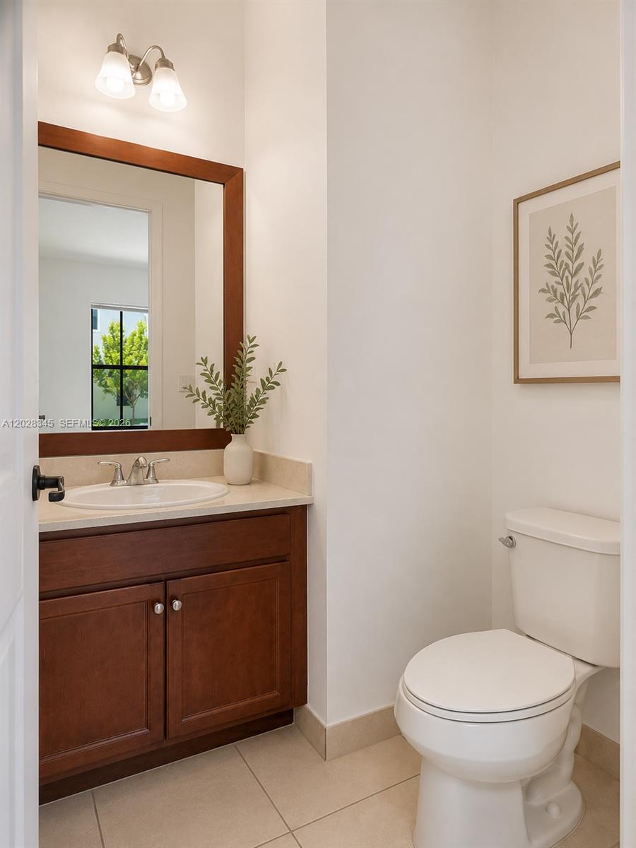 A small bathroom features a wooden vanity, a mirror, a toilet, and framed wall art — 9717 W 34th Ln, Hialeah FL 33018, HIALEAH, FL
