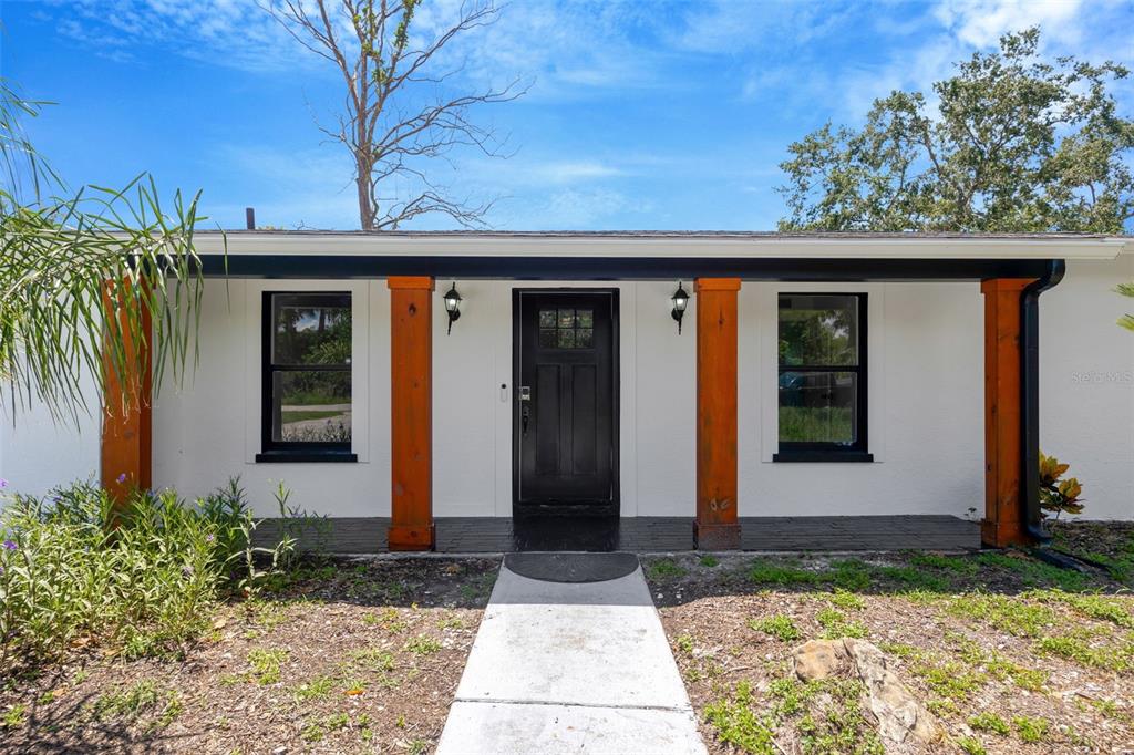 The exterior of a white house features a covered porch with wooden support columns — 9935 RIVER DRIVE, GIBSONTON, FL