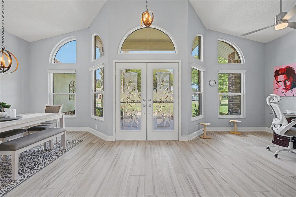 A bright room with light wood floors, vaulted ceilings, and double glass-paneled entry doors — 6207 HUNTINGTON DRIVE, ZEPHYRHILLS, FL