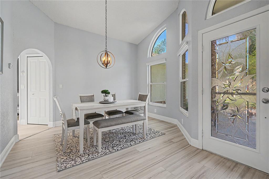 A dining area with a vaulted ceiling, light wood floors, and a decorative glass front door — 6207 HUNTINGTON DRIVE, ZEPHYRHILLS, FL