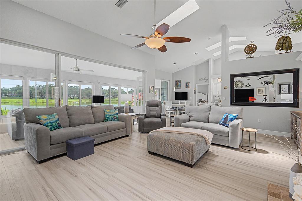 A spacious living room features light wood flooring, a vaulted ceiling, and a large sliding door — 6207 HUNTINGTON DRIVE, ZEPHYRHILLS, FL