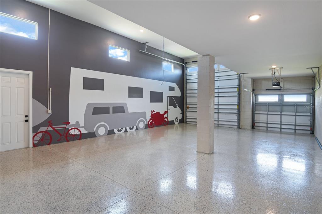 A spacious garage with a mural, epoxy flooring, and two large overhead doors — 190 BLUE STAR COURT, TAVARES, FL