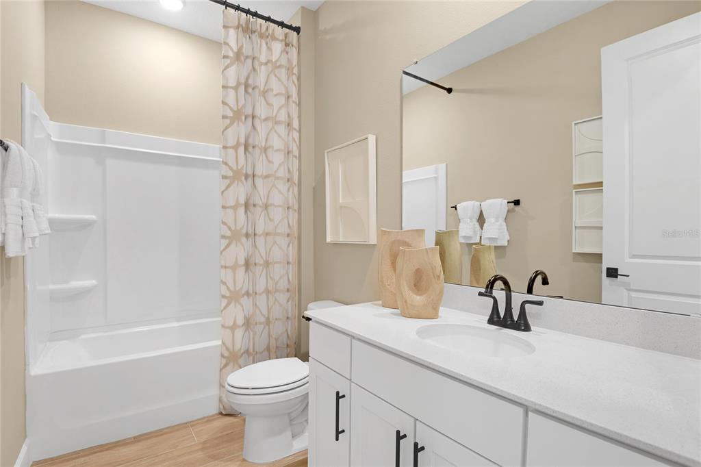 A bathroom features a white vanity, a tub-shower combination, and light-colored wood-look flooring — 190 BLUE STAR COURT, TAVARES, FL