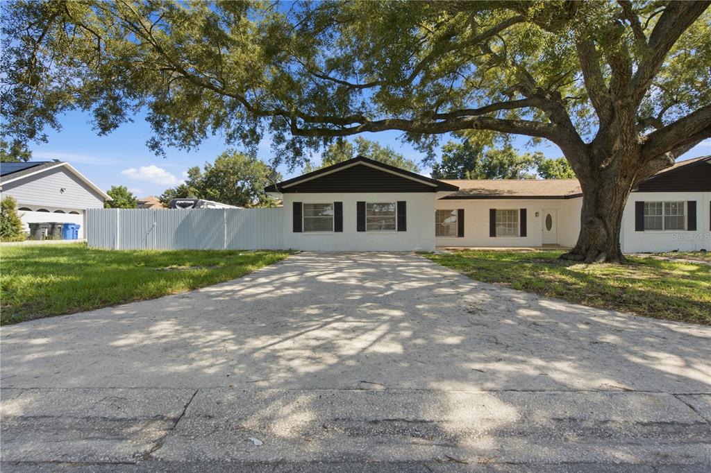 A white single-story house with black shutters sits behind a large tree and driveway — 604 ROYAL CREST DRIVE, BRANDON, FL
