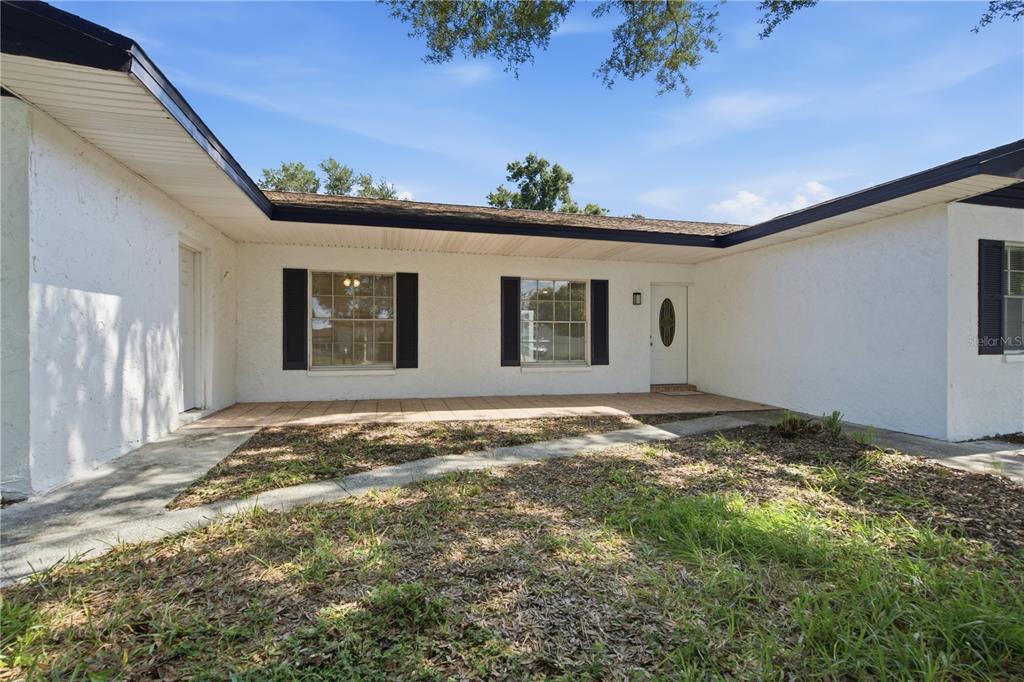 A white stucco house exterior features a covered porch, two windows with shutters, and a door — 604 ROYAL CREST DRIVE, BRANDON, FL
