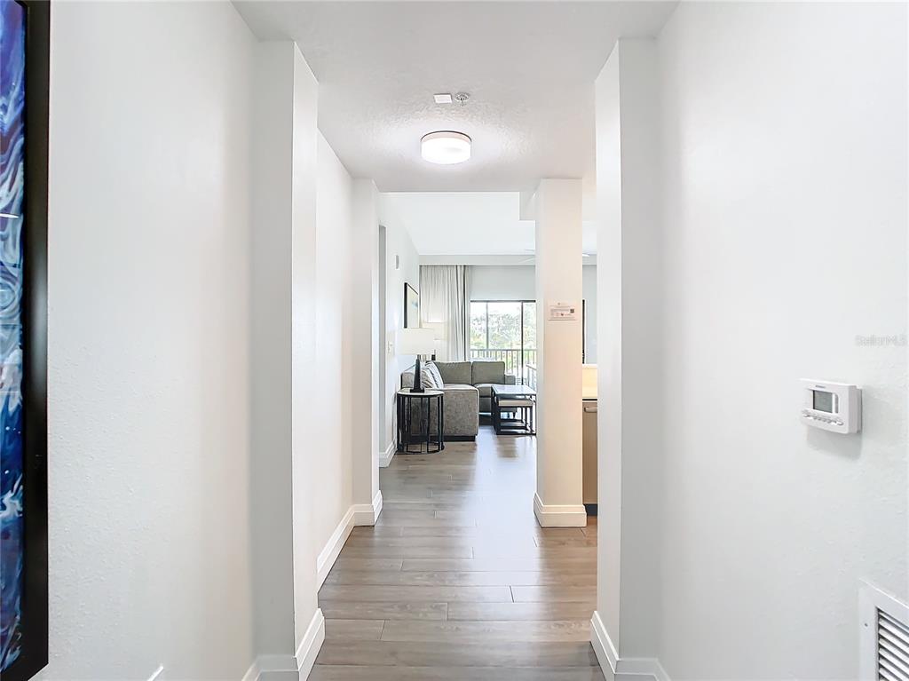 A hallway with wood-look flooring leads into a living room with a gray sectional sofa — 14501 GROVE RESORT AVENUE UNIT 3327, WINTER GARDEN, FL