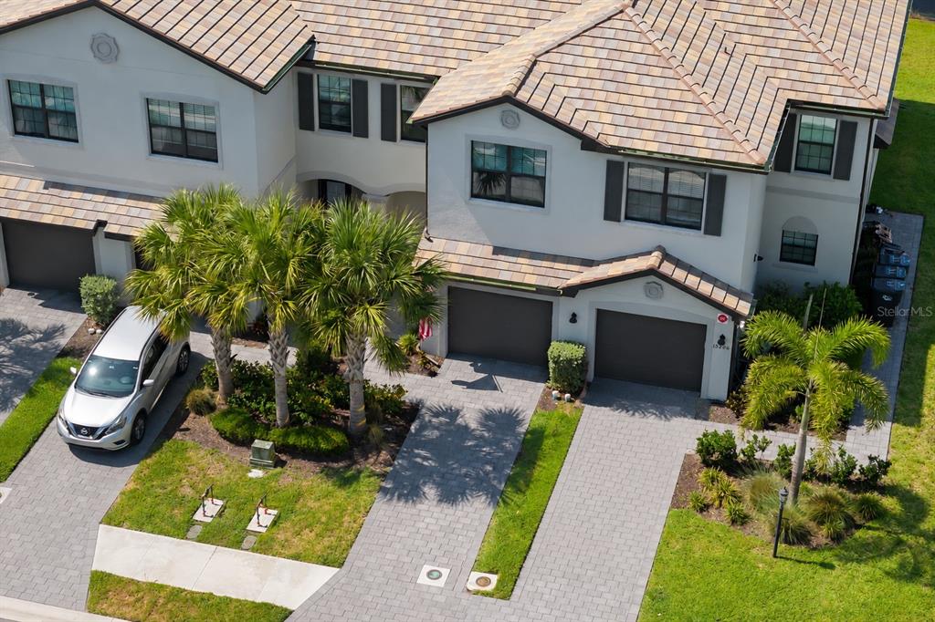 A two-story townhouse exterior features a gray garage door, a paved driveway, and an American flag — 15210 SUNNY DAY DRIVE, BRADENTON, FL
