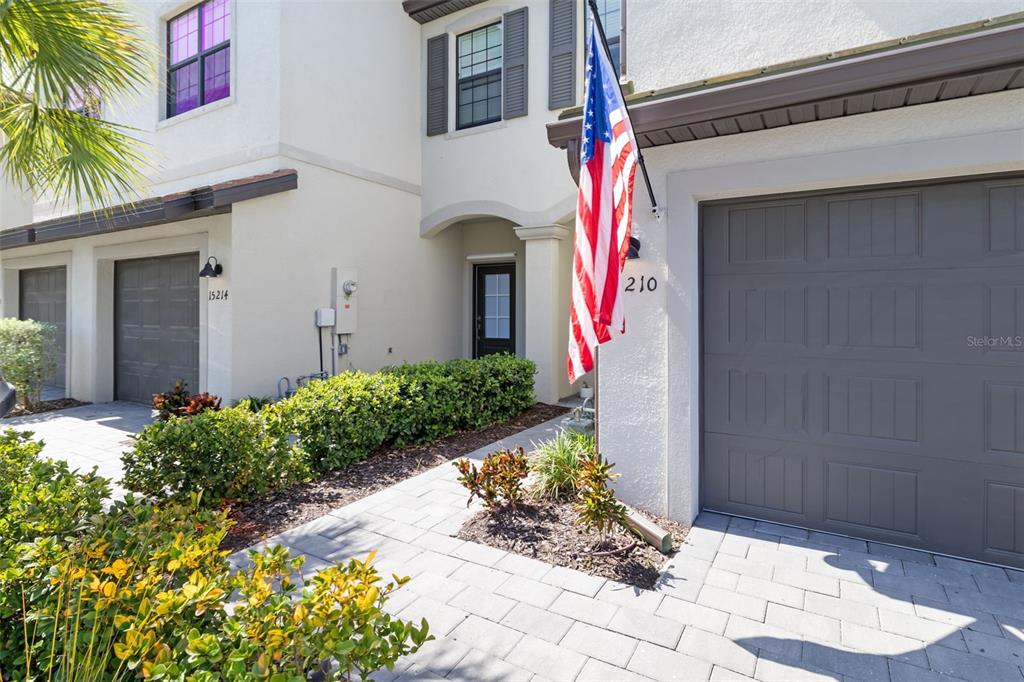 A residential townhouse exterior features a grey garage door, a front entrance, and an American flag — 15210 SUNNY DAY DRIVE, BRADENTON, FL