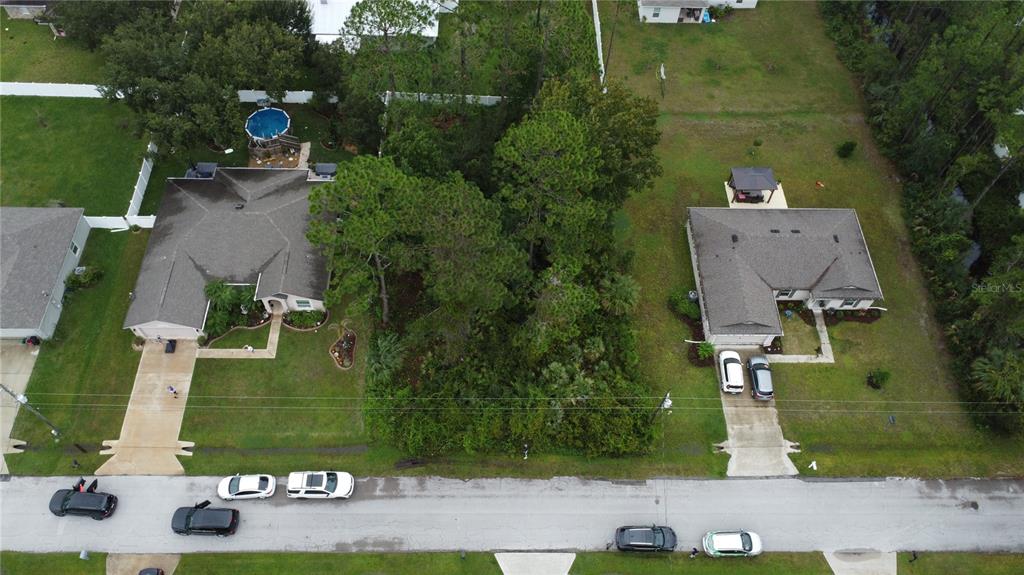An aerial view shows two houses separated by a wooded, undeveloped lot on a street — 24 FORSYTHE LANE, PALM COAST, FL