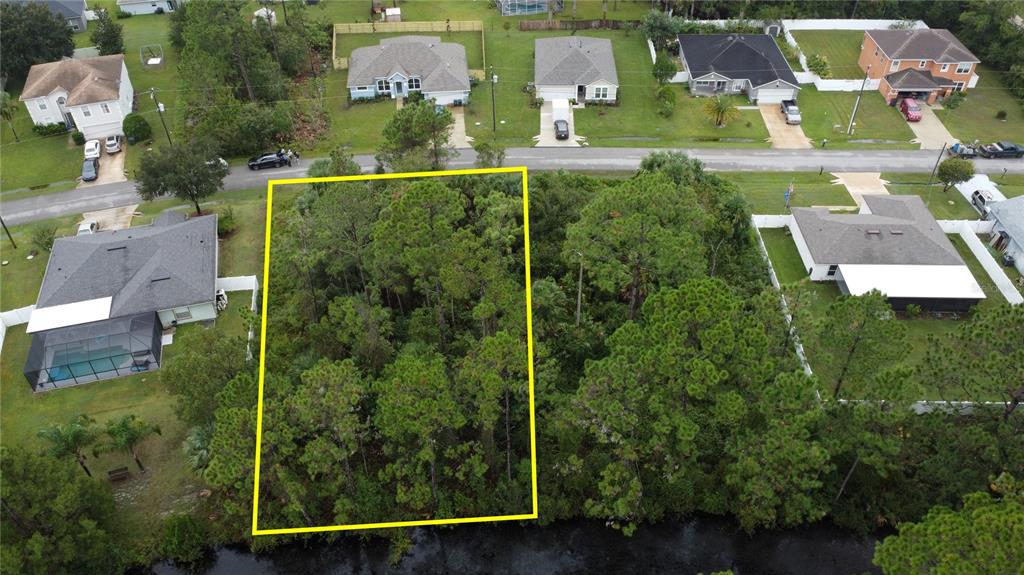 An aerial view shows a wooded, rectangular vacant lot situated between two residential houses — 24 FORSYTHE LANE, PALM COAST, FL