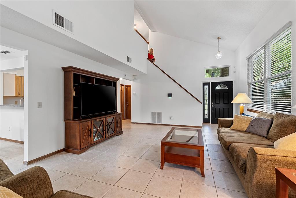 A living room features tile flooring, a vaulted ceiling, a staircase, and brown furniture — 5305 DENVER DRIVE, ORLANDO, FL