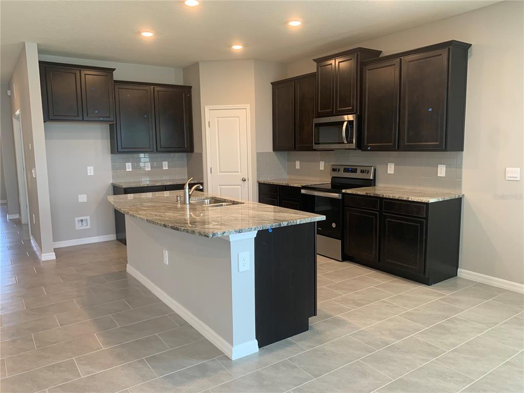 A kitchen features dark wood cabinets, granite countertops, a center island, and light tile flooring — 2012 MIDNIGHT PEARL DRIVE, SARASOTA, FL