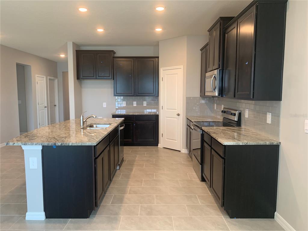 A kitchen features dark wood cabinets, granite countertops, a center island, and light tile flooring — 2012 MIDNIGHT PEARL DRIVE, SARASOTA, FL