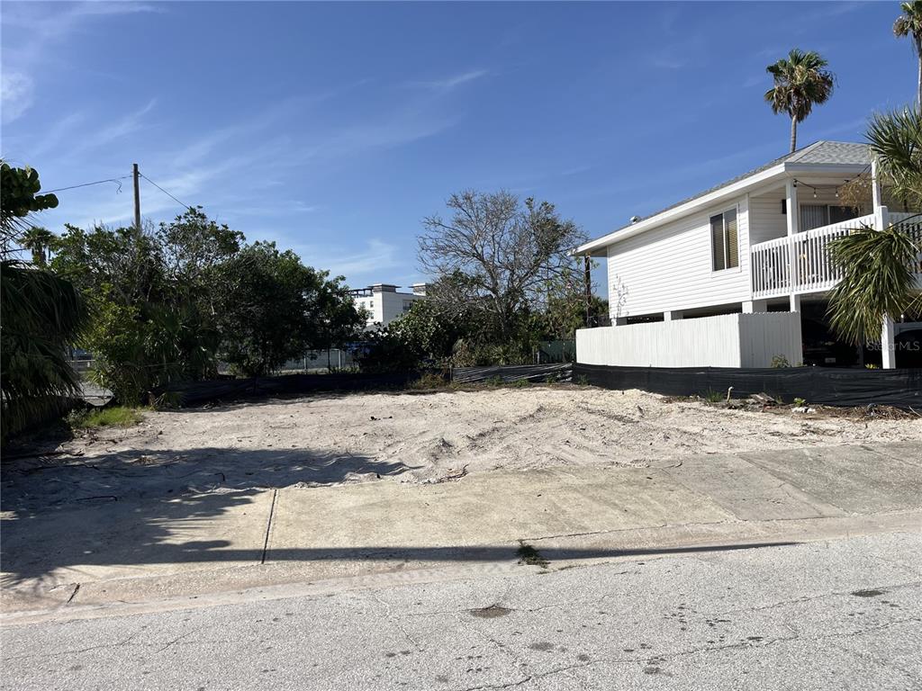 A vacant, sandy residential lot sits next to a two-story white house — 180 E MADEIRA AVENUE, MADEIRA BEACH, FL