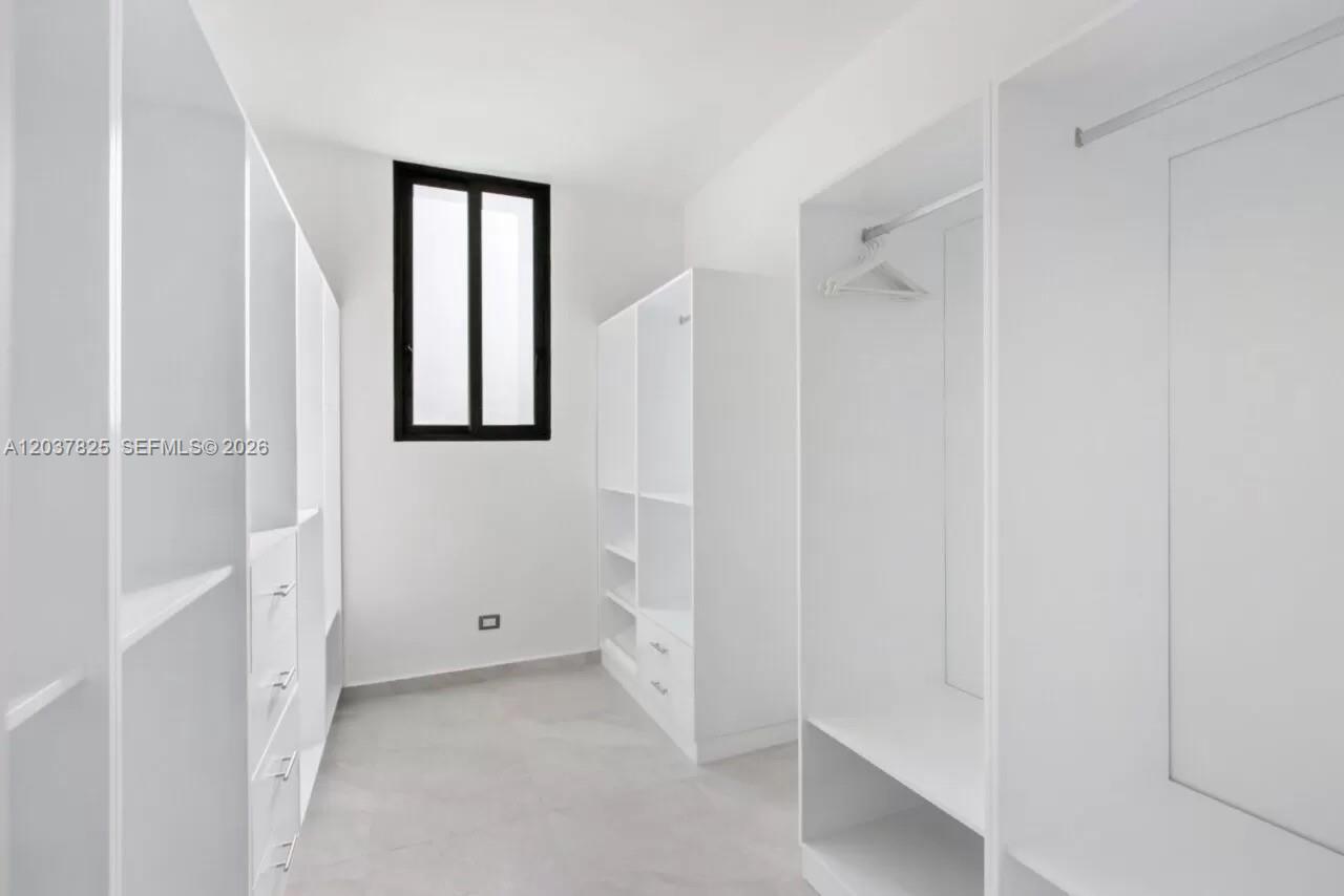 A walk-in closet features white built-in cabinetry, tiled floors, and a single window — 0 l palmas, FL