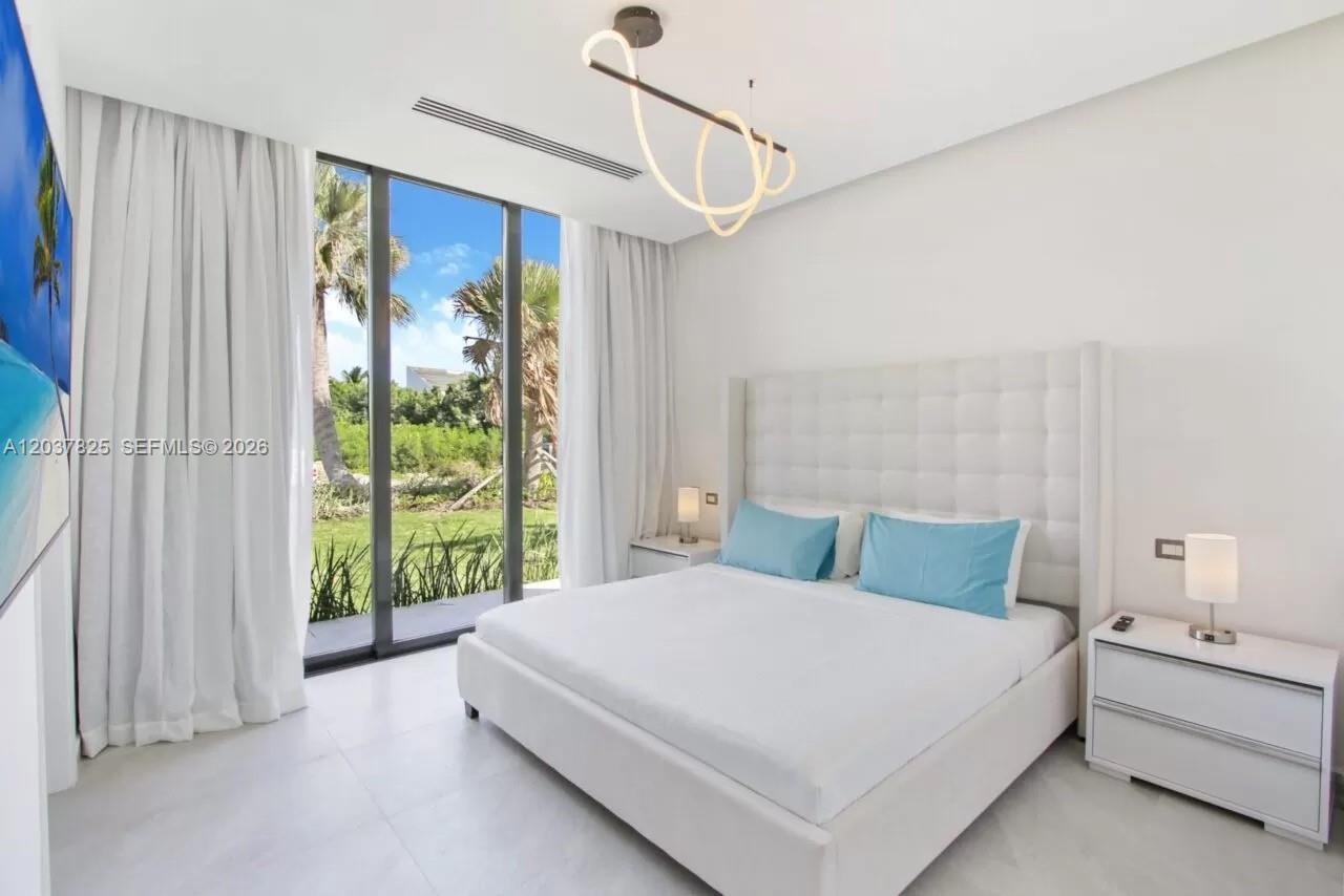 A modern bedroom features a white tufted headboard, blue pillows, and floor-to-ceiling windows — 0 l palmas, FL