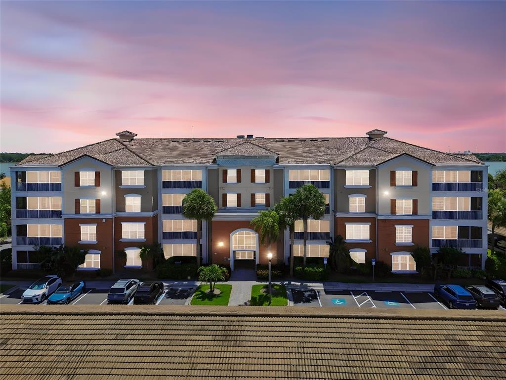 A multi-story apartment building with a tiled roof and parking lot at sunset — 7903 SEMINOLE BOULEVARD UNIT 2401, SEMINOLE, FL