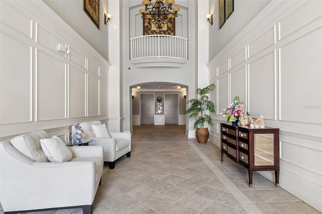 A bright, high-ceilinged lobby features white paneled walls, two armchairs, and a mirrored console table — 7903 SEMINOLE BOULEVARD UNIT 2401, SEMINOLE, FL