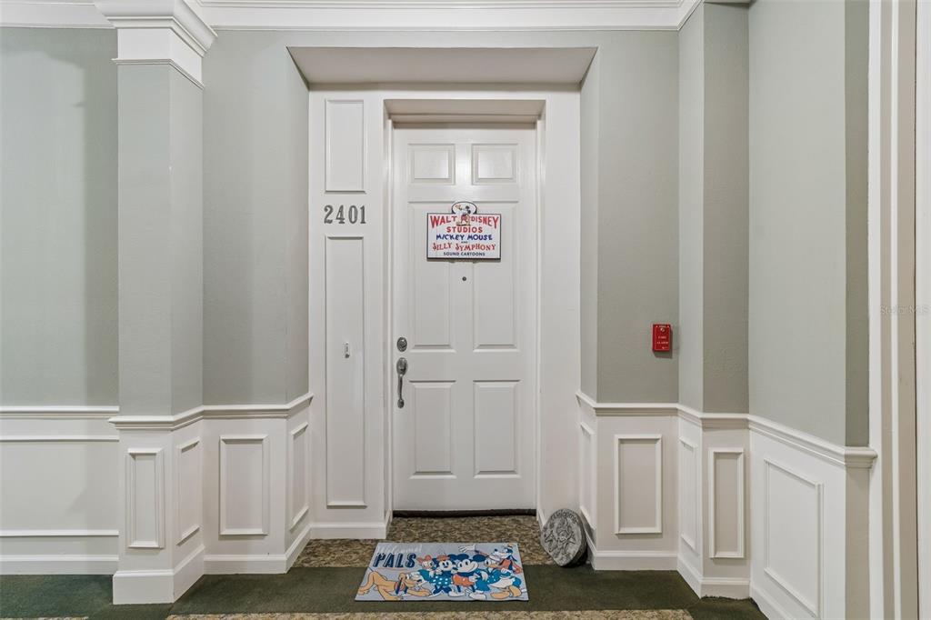 A white front door with a Disney sign and character mat is set in a hallway — 7903 SEMINOLE BOULEVARD UNIT 2401, SEMINOLE, FL