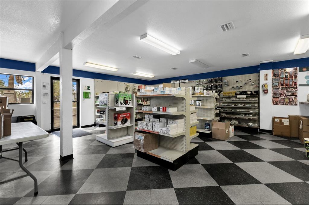 A commercial retail space features checkered flooring, white shelving units, and fluorescent ceiling lights — 18230 PAULSON DRIVE, PORT CHARLOTTE, FL
