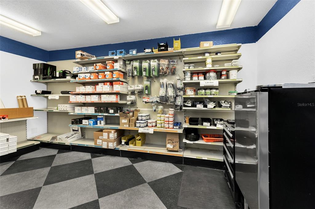 A storage room features white walls with blue trim, metal shelving units, and checkered flooring — 18230 PAULSON DRIVE, PORT CHARLOTTE, FL