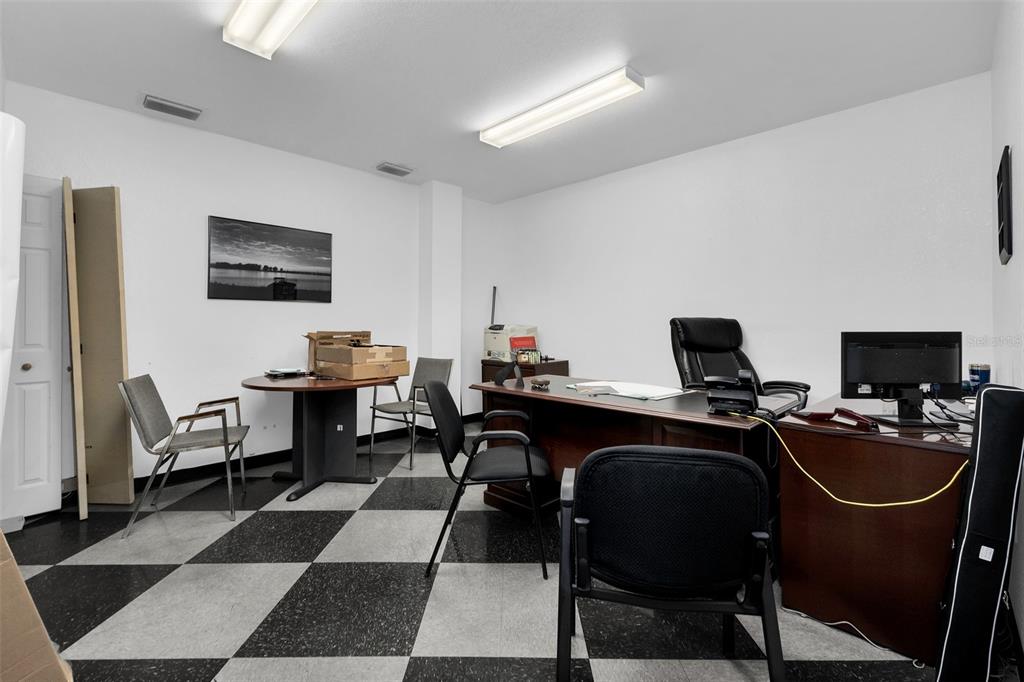 An office space features a checkered floor, two desks, several chairs, and fluorescent lighting — 18230 PAULSON DRIVE, PORT CHARLOTTE, FL