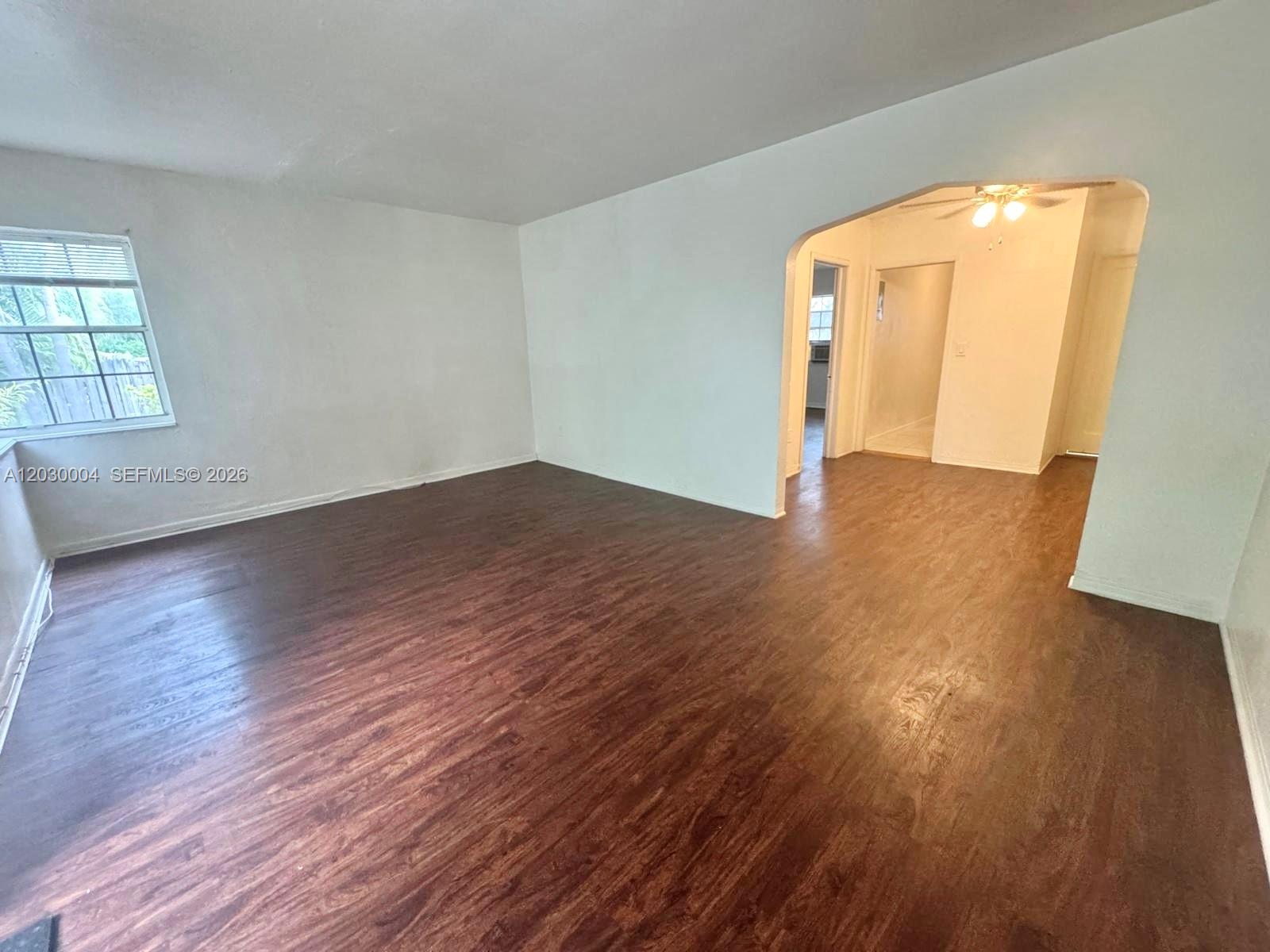 An empty room features dark wood-look flooring, white walls, and an arched entryway — 4410 NE 2nd Ave # 4414, Miami FL 33137, MIAMI, FL
