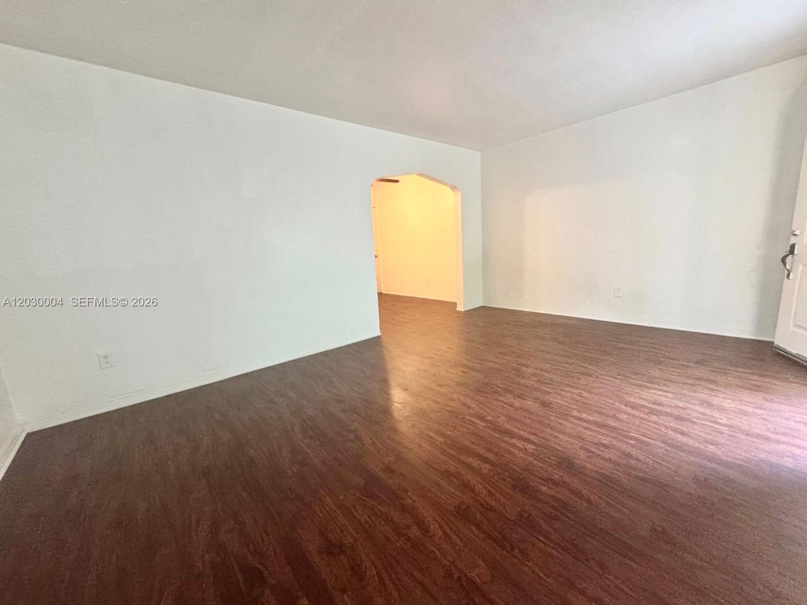 An empty room features white walls, dark wood-look flooring, and an arched doorway — 4410 NE 2nd Ave # 4414, Miami FL 33137, MIAMI, FL