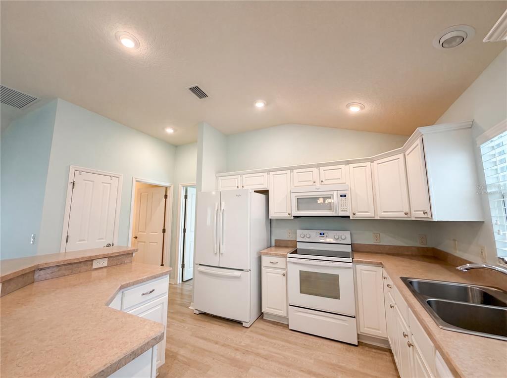 A kitchen features white cabinets, white appliances, and tan countertops with a double sink — 3323 ABANA PATH, THE VILLAGES, FL