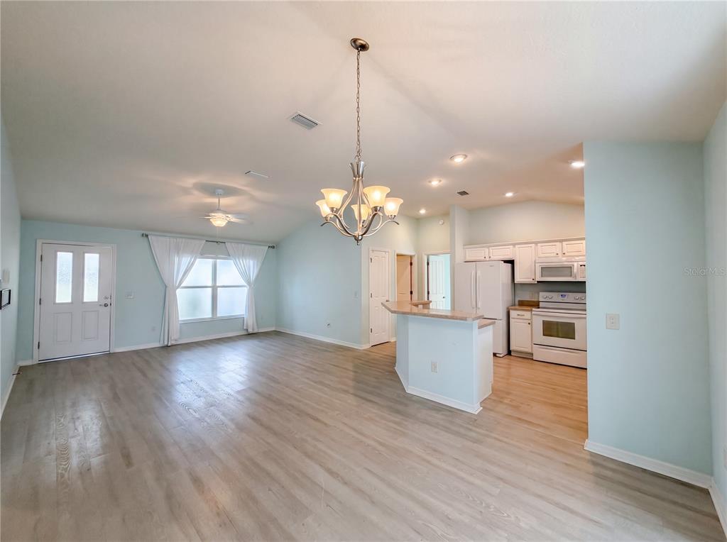 An open-concept living area features light wood flooring, a kitchen island, and a dining chandelier — 3323 ABANA PATH, THE VILLAGES, FL