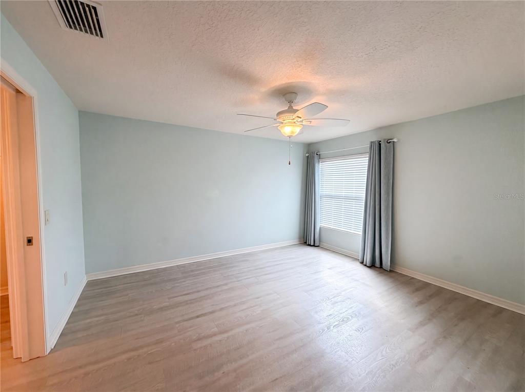 An empty bedroom features light blue walls, wood-look flooring, a ceiling fan, and window curtains — 3323 ABANA PATH, THE VILLAGES, FL