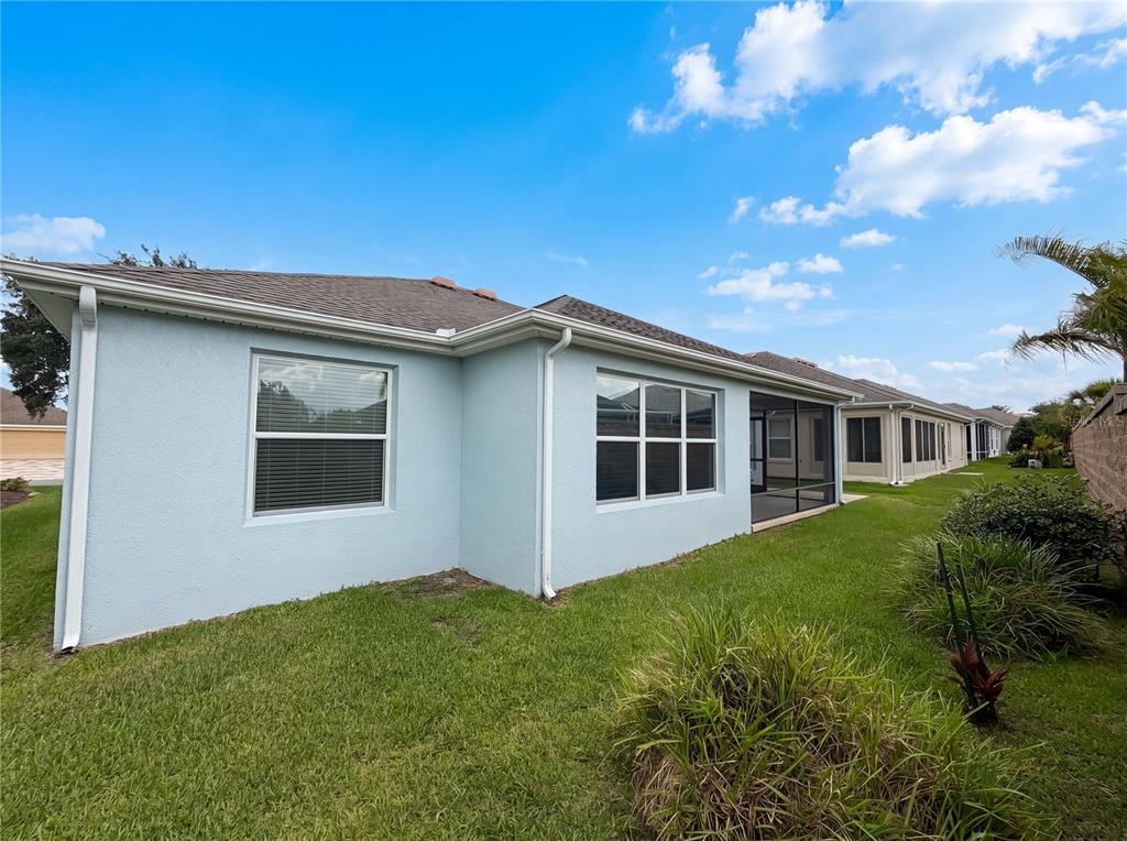The exterior of a light blue house features a screened-in lanai and a grassy backyard — 3323 ABANA PATH, THE VILLAGES, FL
