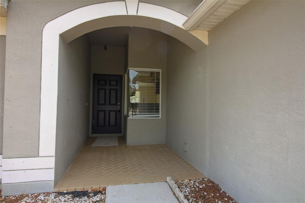 A covered entryway features a dark front door, a window, and light-colored brick flooring — 1702 HOLTON ROAD, LAKELAND, FL