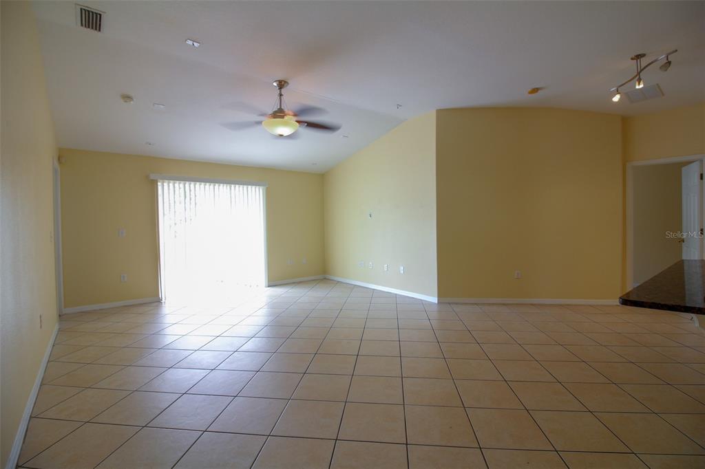 An empty living room features light yellow walls, tile flooring, a ceiling fan, and sliding doors — 1702 HOLTON ROAD, LAKELAND, FL
