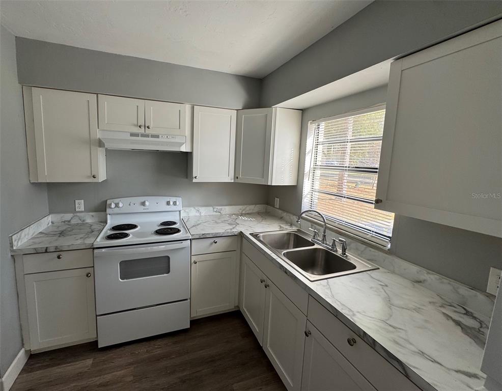 A kitchen features white cabinets, marble-patterned countertops, a white stove, and a stainless steel sink — 7130 SW 45TH PLACE UNIT B, GAINESVILLE, FL