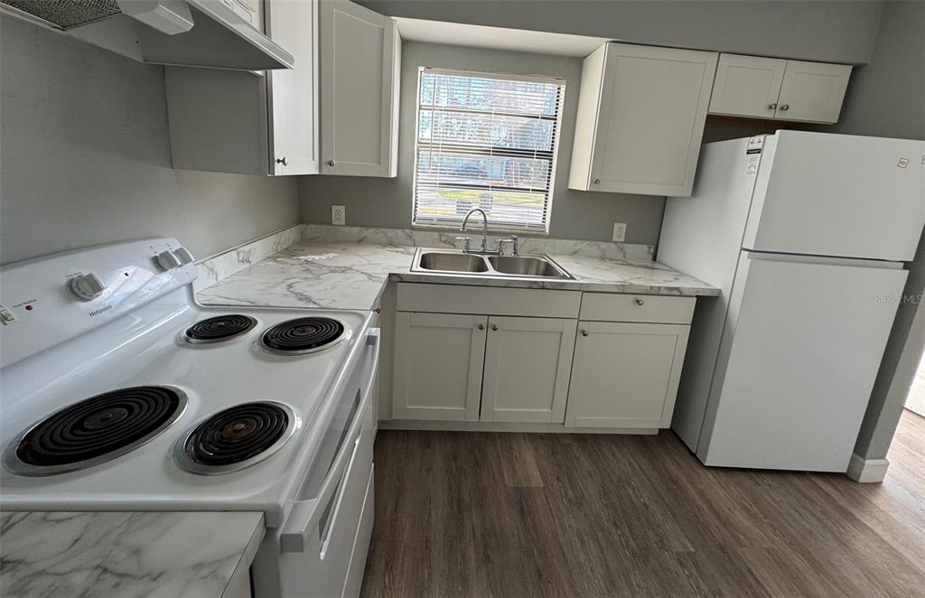 A kitchen features white cabinets, marble-look countertops, a white stove, and a white refrigerator — 7130 SW 45TH PLACE UNIT B, GAINESVILLE, FL