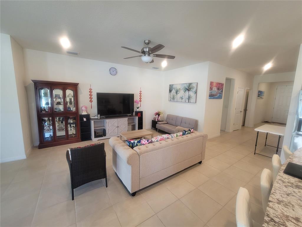 A living room features a beige sofa, a dark armchair, a television console, and tile flooring — 7238 STEER BLADE DRIVE, ZEPHYRHILLS, FL