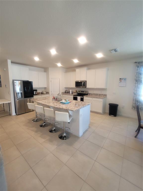 A kitchen features white cabinetry, granite countertops, a central island with bar seating, and appliances — 7238 STEER BLADE DRIVE, ZEPHYRHILLS, FL