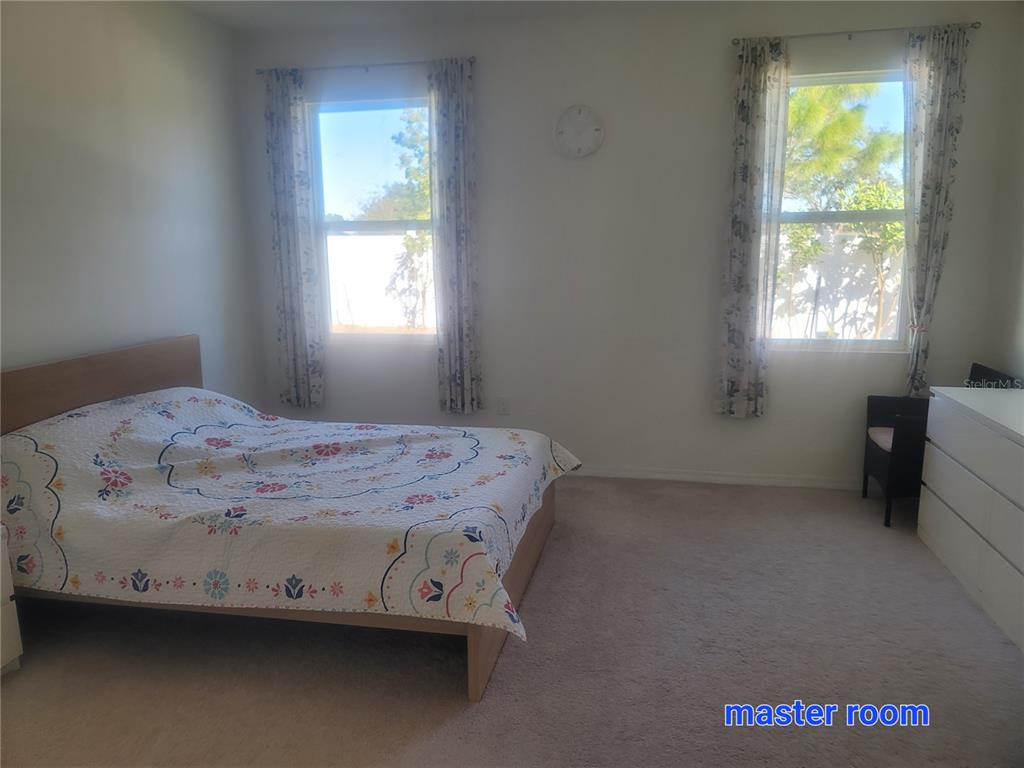 A bedroom with a bed, two windows with curtains, and a dresser on carpeted flooring — 7238 STEER BLADE DRIVE, ZEPHYRHILLS, FL