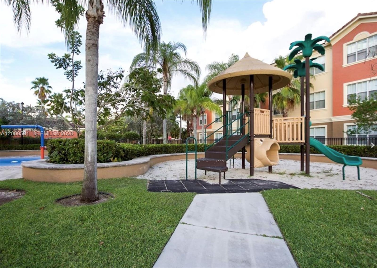 A playground with a slide and climbing structure sits on a sand base near apartments — 4508 SW 160th Ave # 736, Miramar FL 33027, MIRAMAR, FL