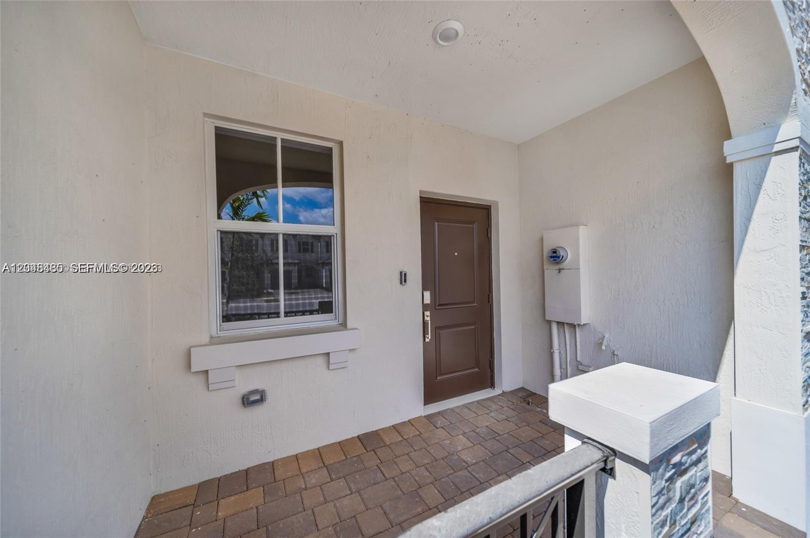 This exterior view shows a covered entryway with a brown door, a window, and pavers — 12918 NW 23rd Pl, Miami FL 33167, MIAMI, FL