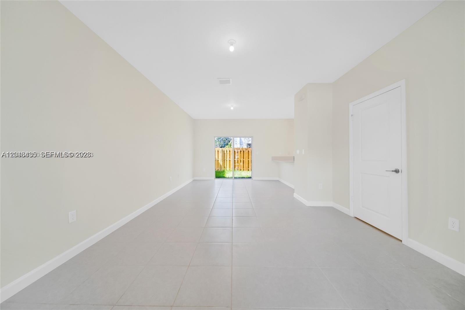 An empty room with light-colored walls, tile flooring, and a sliding glass door to outside — 12918 NW 23rd Pl, Miami FL 33167, MIAMI, FL