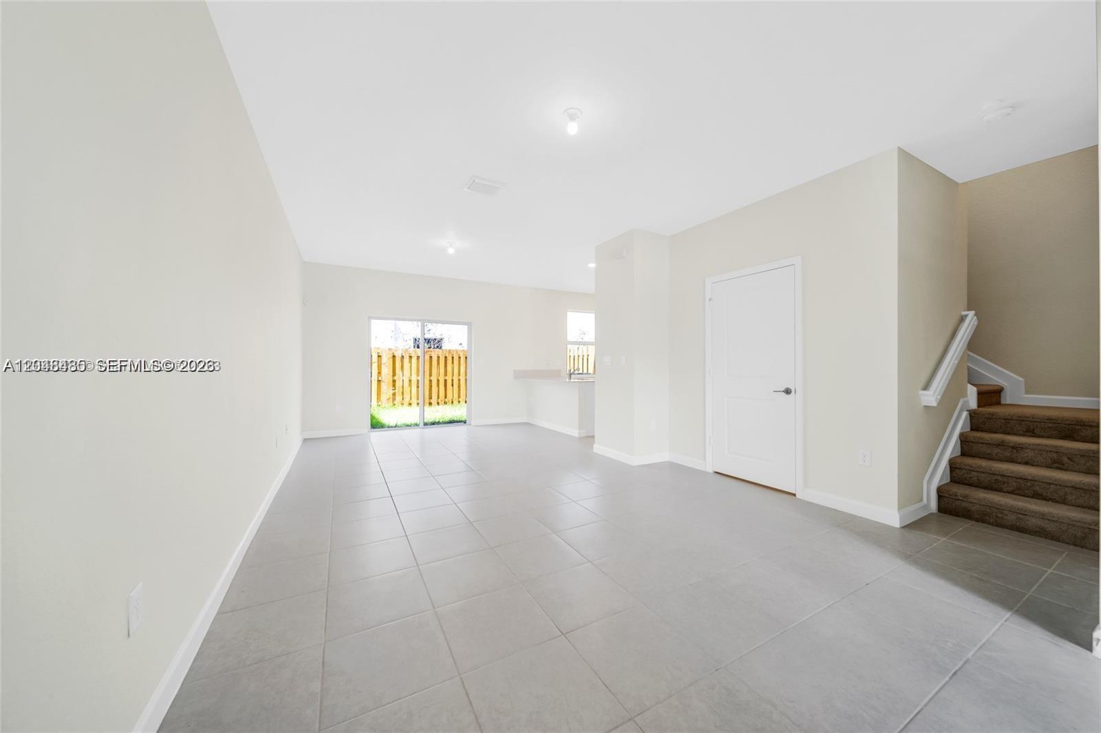 An open-concept living area features light tile flooring, a staircase, and a sliding glass door — 12918 NW 23rd Pl, Miami FL 33167, MIAMI, FL