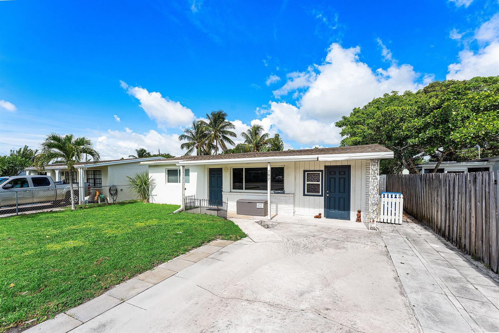 A single-story white house with a concrete driveway, lawn, and palm trees under a blue sky — 707 S Broadway, Lantana FL 33462, LANTANA, FL