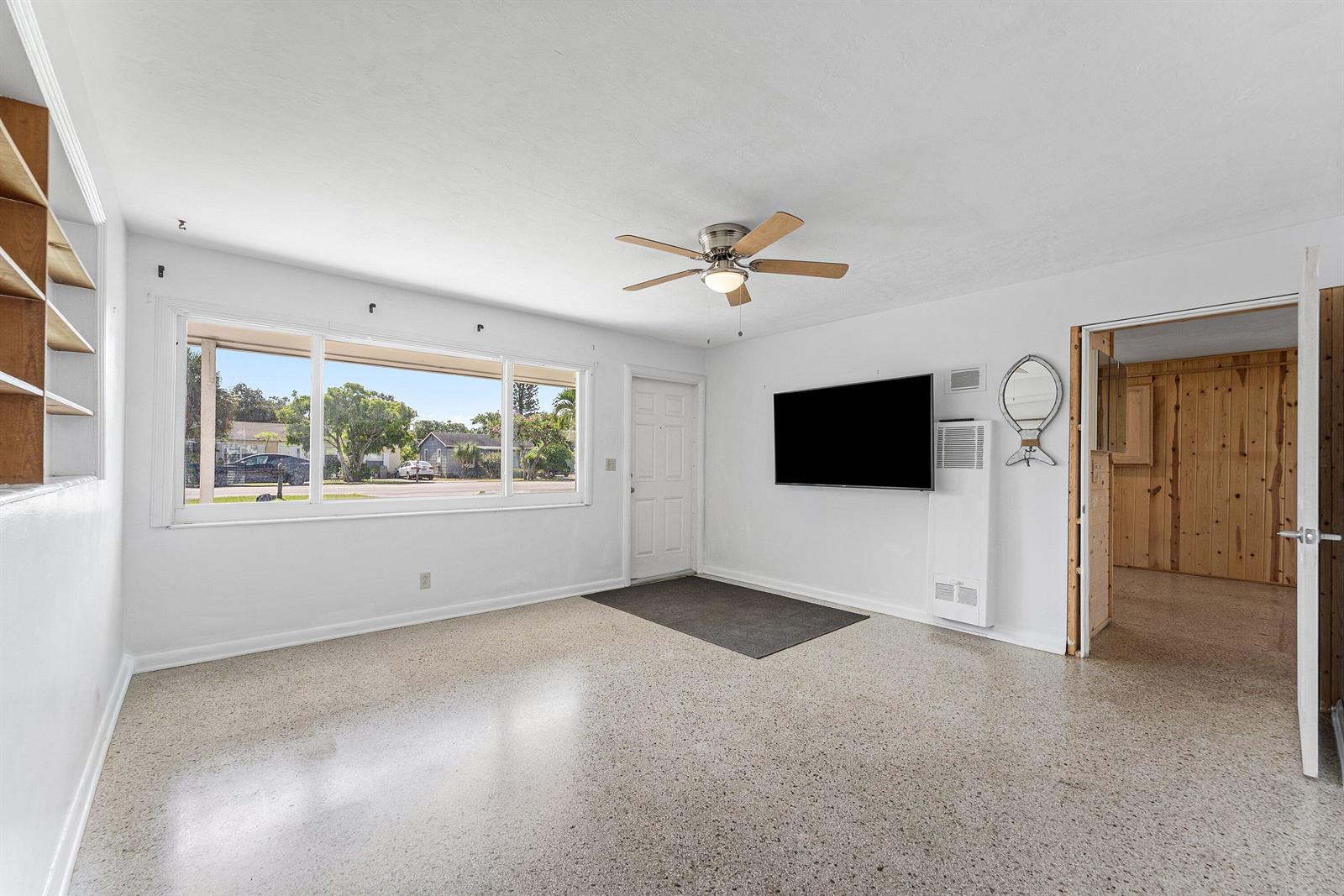 A living room with a ceiling fan, large window, wall-mounted television, and terrazzo flooring — 707 S Broadway, Lantana FL 33462, LANTANA, FL