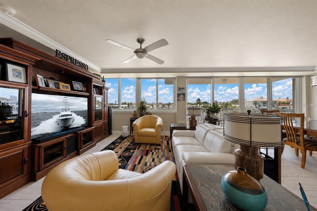 A living room features a large entertainment center, white sofa, yellow armchairs, and floor-to-ceiling windows — 223 ISLAND WAY UNIT 2E, CLEARWATER BEACH, FL