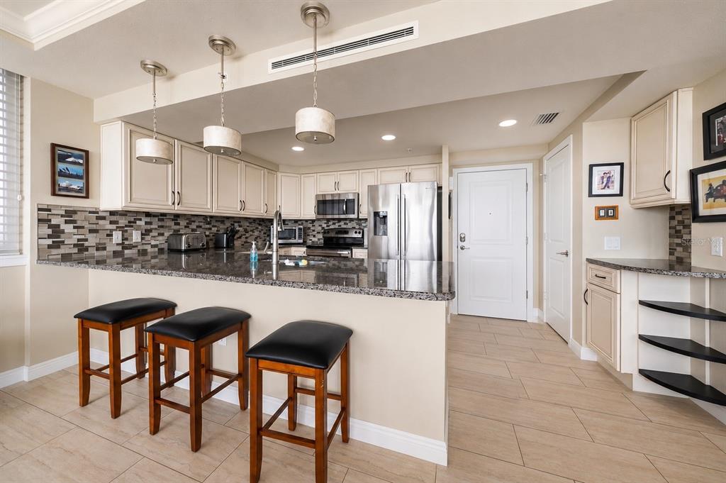 A kitchen with granite countertops, wooden bar stools, stainless steel appliances, and cream-colored cabinetry — 223 ISLAND WAY UNIT 2E, CLEARWATER BEACH, FL