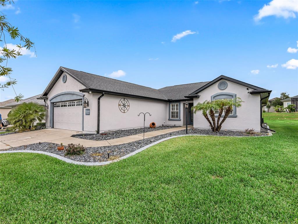 A single-story house with a light-colored stucco exterior, a gray roof, and a paved driveway — 12115 SE 176TH LOOP, SUMMERFIELD, FL