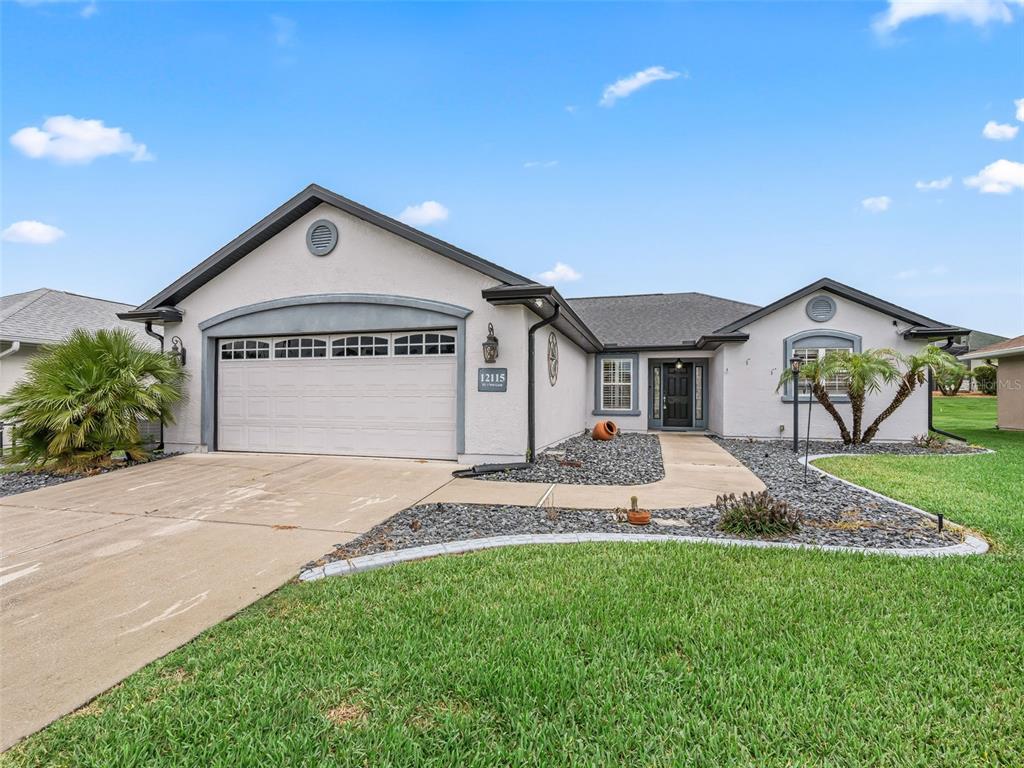 A single-story house with a two-car garage, gray stucco exterior, and a landscaped front yard — 12115 SE 176TH LOOP, SUMMERFIELD, FL